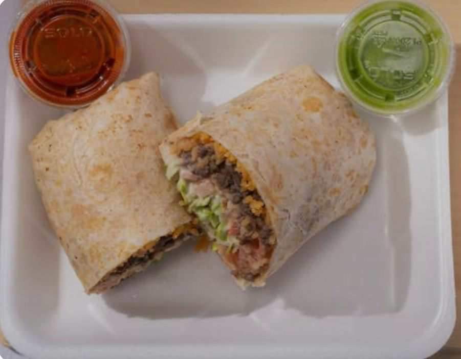 A burrito cut in half beside cups of salsa verde and salsa rojo