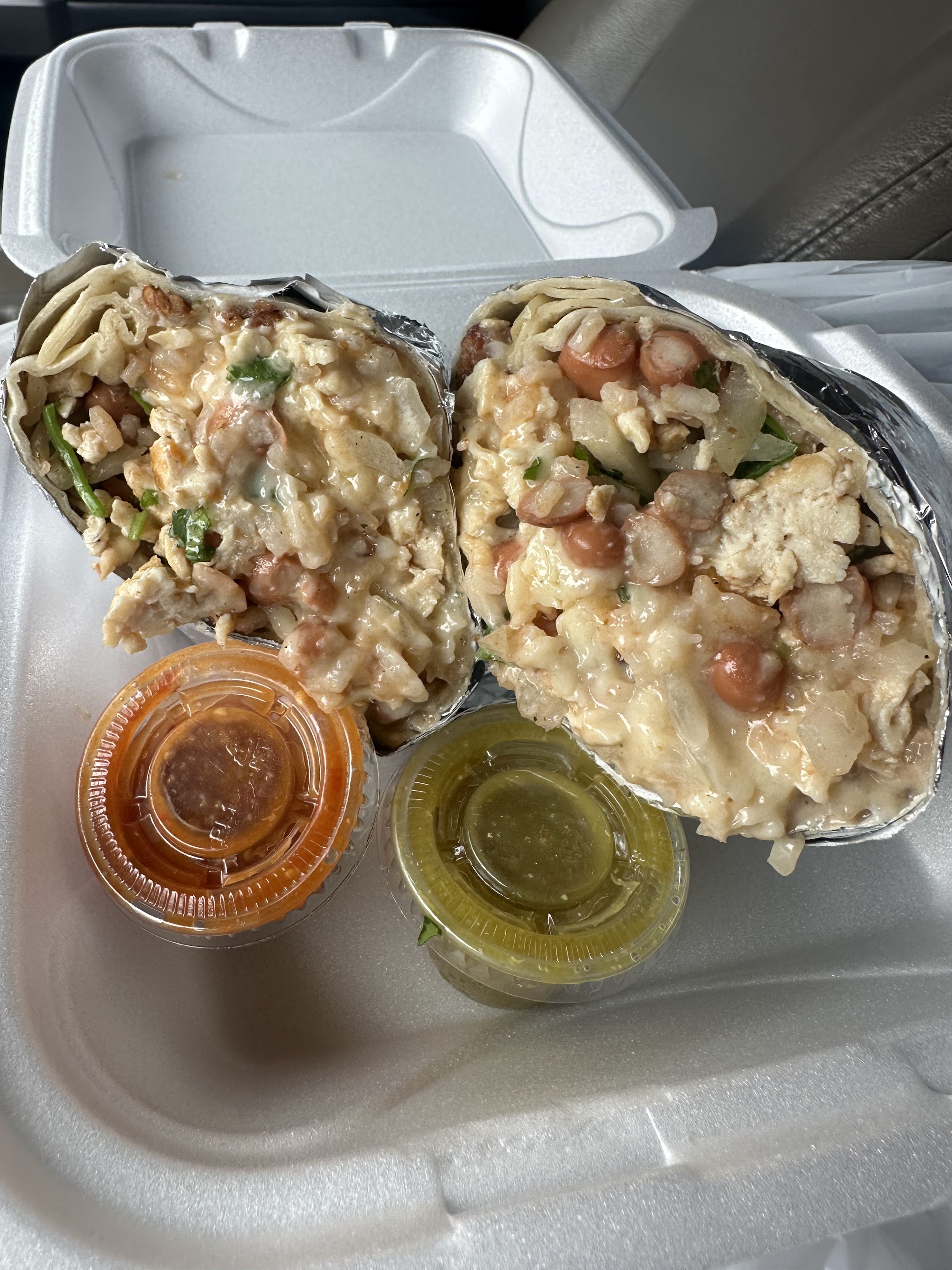 Two burritos with rice and beans in a takeout box